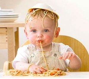 Детето яде макарони и всичко е омазано с тях