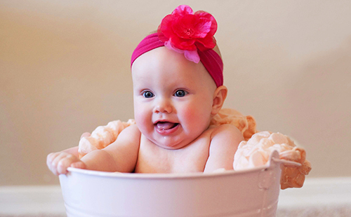 Щастлива малка бебе с червен лък, седящ във вана