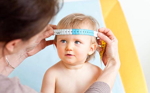 Лекарят измерва обиколката на черепа на детето, за да разбере дали се развива правилно