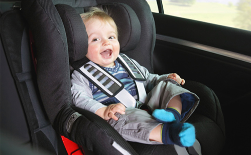 Радостното малко момче седи на столче за кола и очаква пътуването