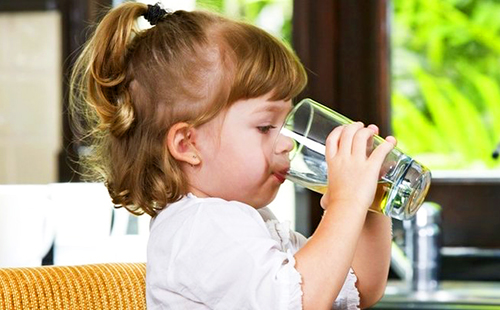 Малкото момиче пие вода от стъклена чаша