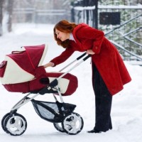 Мама в червено палто ходене с бебе на инвалидна количка през зимата