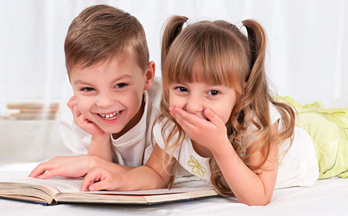 Момче и момиче четат книга и се смеят