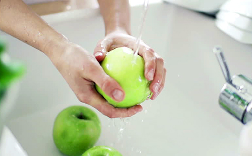 Ръцете внимателно измиват зелените ябълки под кранчето