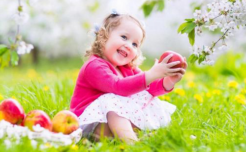 Едно момиче в розова блуза държи ябълка и се смее