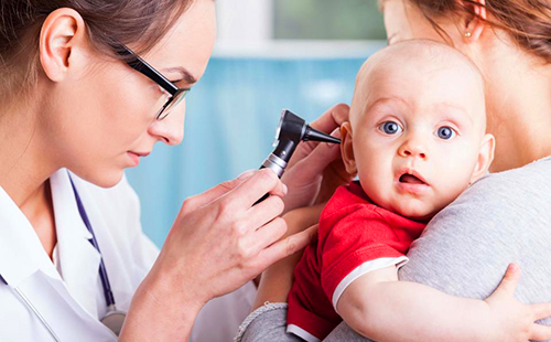 Докторът изследва ухото на бебето в червена фланелка