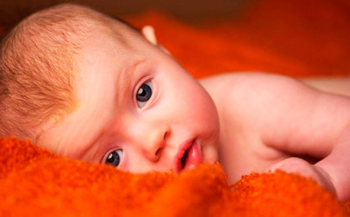 Детето лежи върху оранжево одеяло