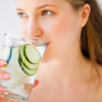 Млада жена пие от чаша вода с парчета краставица
