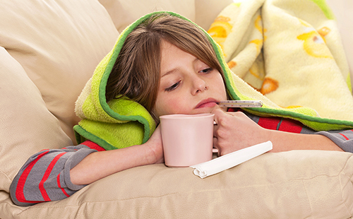 Едно момиче с температура се увива в уютно одеяло и пие чай