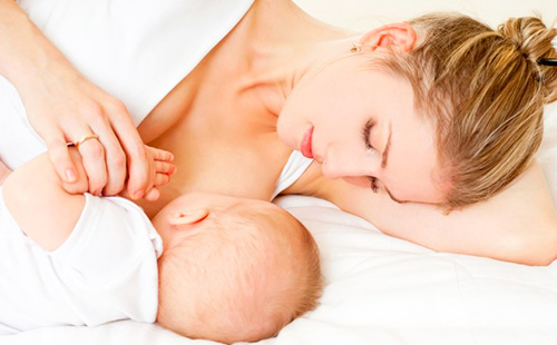 Млада жена, която лежи, кърми бебе