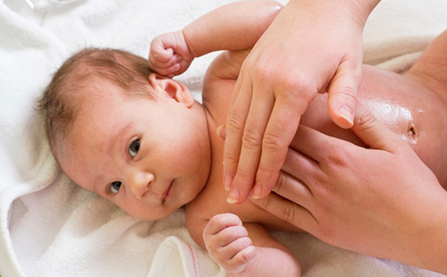 Ръцете на мама нежно извършват дренажен масаж на бебето