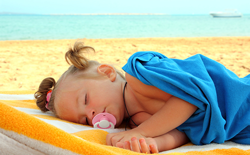 Малко момиче спи на плажа, покрито със сини одеала