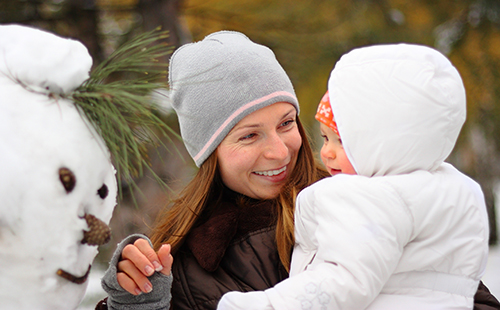 Радостна майка с бебето се възхищава на снежния човек