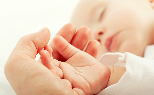Ръката на майка с нежност държи дланта на сънното бебе