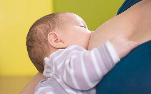 Едно бебе в раиран пуловер суче гърдите на майката