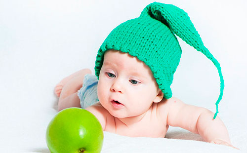 Дете в зелена плетена шапка гледа към ябълка