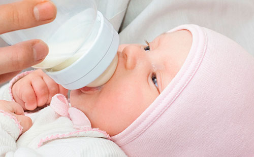 Бебето изсмуква млякото от бутилката