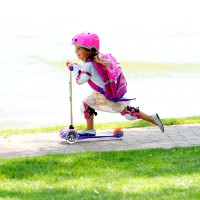 Едно щастливо малко момиче с розова раница се втурва по пътеката на скутера