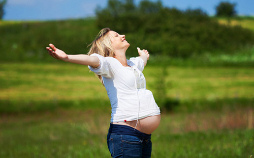 Една щастлива бременна жена разпростря ръце, за да посрещне слънцето