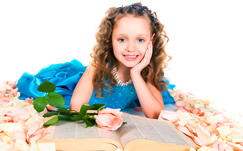 Малка принцеса в синя рокля е подредена с голяма книга сред розите