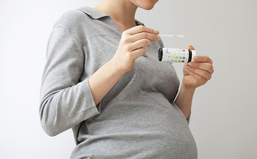 Бременната в сиво държи тест лента за анализ на урината