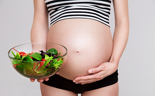 Бременната поддържа чиния със салата