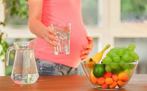 Бременна жена, държаща чаша вода