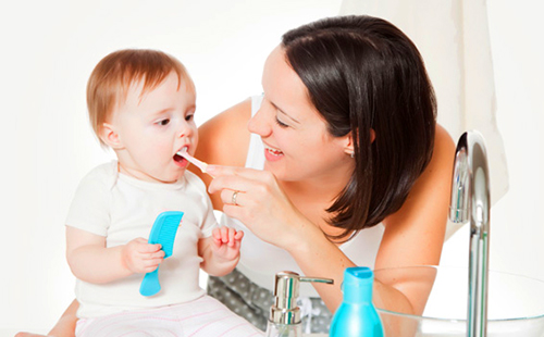Черната коса майка се смее и почиства зъбите на бебето си