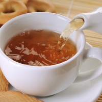 Черният чай се излива от чайник в чаша