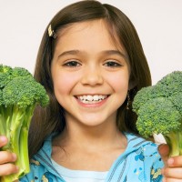 Усмихнатото момиче държи две големи броколи